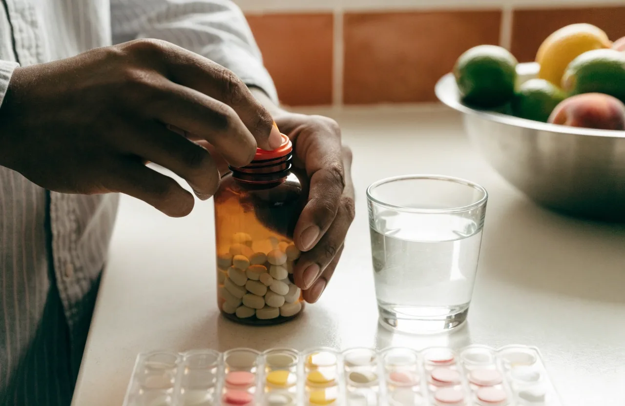 Hombre adulto tomando un suplemento con un vaso de agua en una cocina luminosa